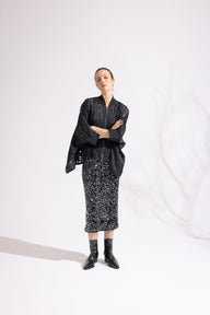 Person wearing a black outfit with a patterned skirt on a white background