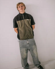Person wearing a black and green jacket with a white wall background