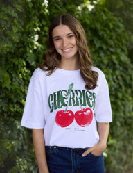 Woman wearing a white t-shirt with red apples and green text against a green leafy background