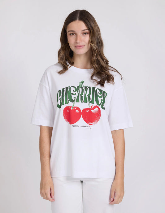 Person wearing a white t-shirt with red cherries and green text on a plain background