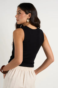 Woman wearing a black sleeveless top and beige pants against a white background