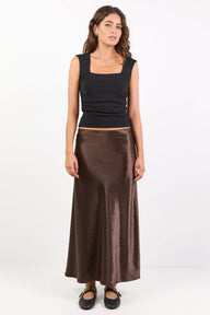 Woman wearing a black top and brown satin skirt on a white background