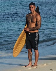 Man with tattoos holding a wooden surfboard on a beach