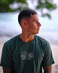 Man wearing a green t-shirt with a logo, sitting by a body of water.