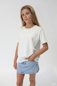 girl wearing an oat marle t-shirt and denim skirt on a plain background