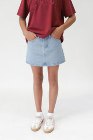 Person wearing a red shirt, light blue denim skirt, and white sneakers on a white background