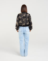 Person wearing a black floral jacket and light blue jeans on a white background
