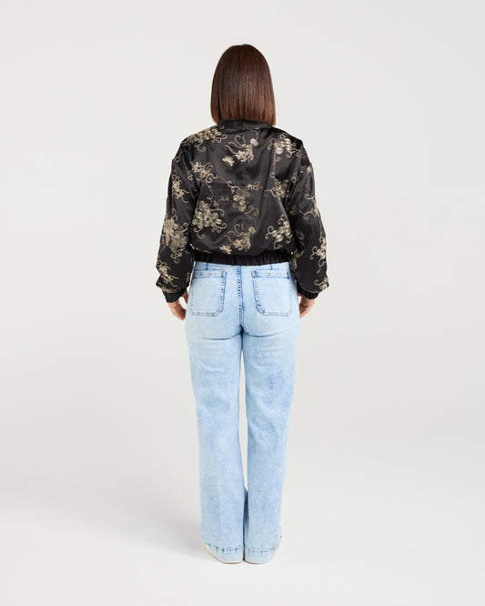Person wearing a black floral jacket and light blue jeans on a white background
