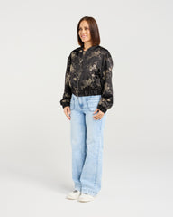 Woman wearing a black floral bomber jacket and light blue jeans on a white background