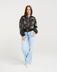 Woman wearing a camouflage bomber jacket and light blue jeans on a white background