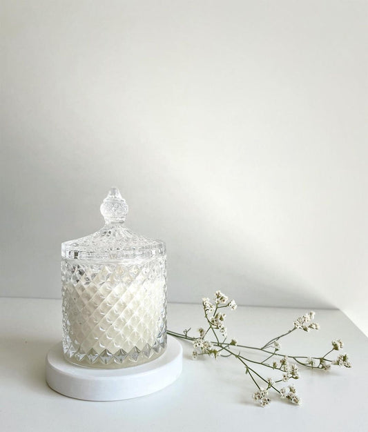 Decorative glass jar with a white candle inside on a white surface with a white background