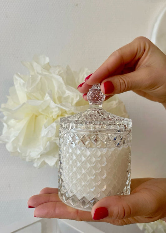 Hand holding a decorative glass container with a white floral background