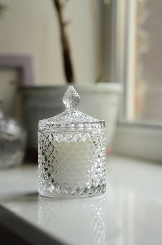 Decorative glass jar with a textured lid on a reflective surface
