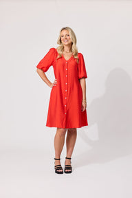 A woman modeling a bright red short-sleeve button-front dress with a V-neck and knee-length skirt, standing against a plain light gray studio background.