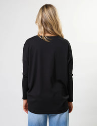 Person wearing a black long-sleeve top and blue jeans on a white background