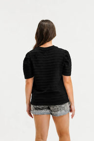 Person wearing a black t-shirt and patterned shorts on a white background