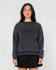 Woman wearing a dark gray sweatshirt with a logo on a plain background