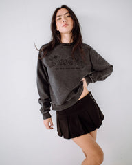 Woman wearing a dark gray sweatshirt with text and a black pleated skirt on a white background
