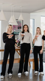 Three women standing in a modern kitchen holding drinks.