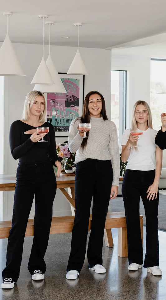Three women standing in a modern kitchen holding drinks.