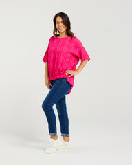 Woman wearing a bright pink top and blue jeans on a white background
