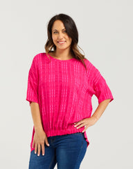 Woman wearing a bright pink top and blue jeans on a white background