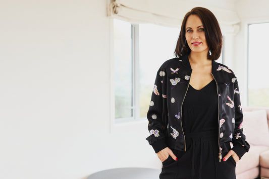 Woman wearing a black bomber jacket with butterfly patterns in a bright room.