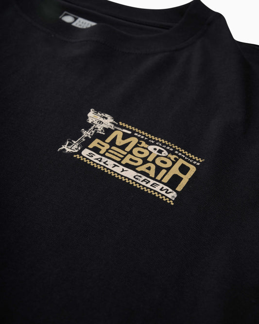 Close-up of a black crewneck t-shirt featuring a distressed gold and white graphic on the left chest that reads 'Motor Repair Salty Crew' with a wrench illustration.