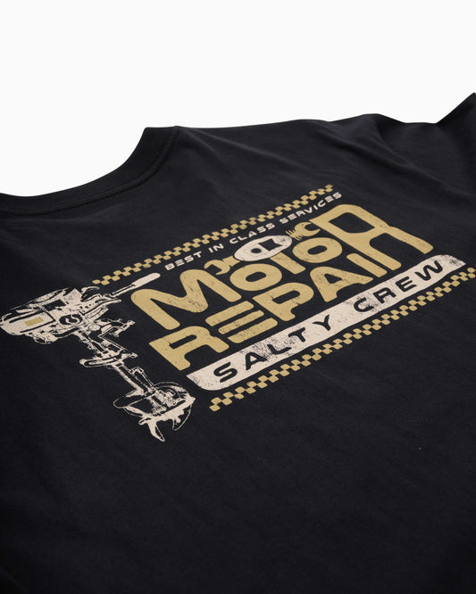 Close-up of a black crewneck t-shirt featuring a distressed gold and white graphic on the left chest that reads 'Motor Repair Salty Crew' with a wrench illustration.