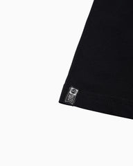 Close-up of a black garment corner with a small rectangular sewn label reading 'salty crew' and a circular logo, shown on a plain white background.