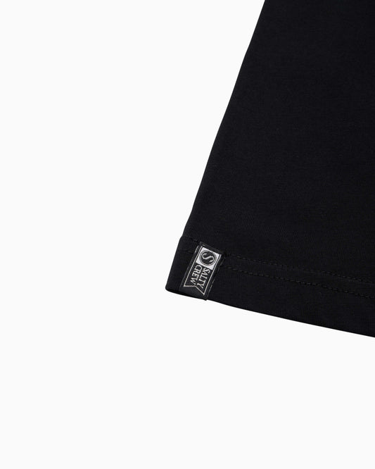 Close-up of a black garment corner with a small rectangular sewn label reading 'salty crew' and a circular logo, shown on a plain white background.