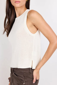 A woman wearing a ribbed knit sleeveless top in off-white, paired with dark brown corduroy pants, shown from the side against a plain light background.