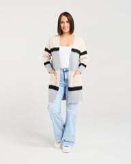 Woman wearing a long, patterned cardigan over a white top and light blue jeans on a plain background