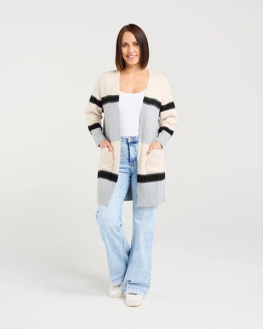 Woman wearing a long, patterned cardigan over a white top and light blue jeans on a plain background