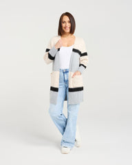 Woman wearing a long, patterned cardigan over a white top and light blue jeans on a white background