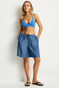 Woman wearing a blue bikini top and denim shorts on a white background