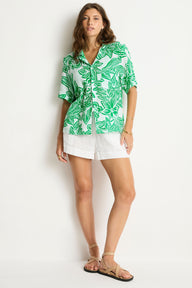 Woman wearing a green leaf-patterned shirt and white shorts on a white background