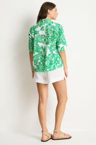 Woman wearing a green floral shirt and white shorts against a white background