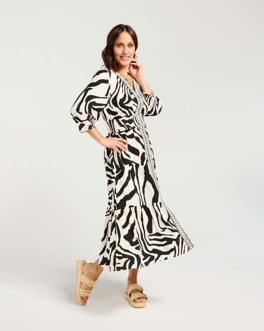 A woman modeling a long-sleeved maxi dress with a bold black and white zebra print, standing against a light gray studio background.