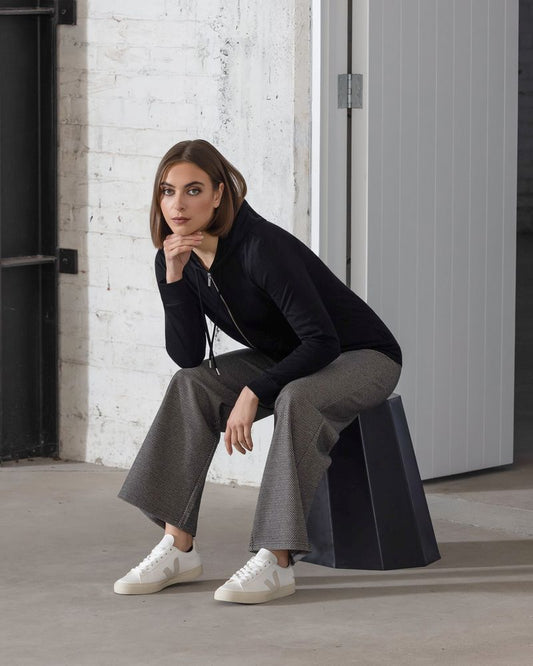Woman sitting on a black stool against a white brick wall.