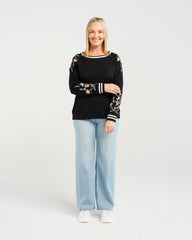 Woman wearing a black sweater with floral designs and light blue jeans on a white background