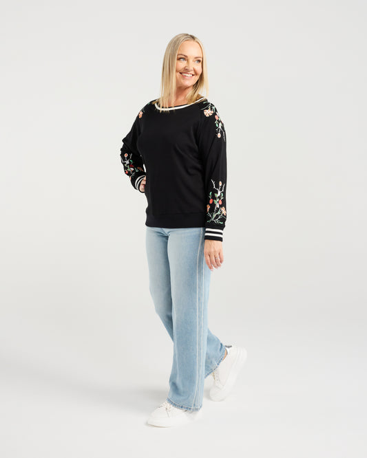 Woman wearing a black sweater with floral patterns and light blue jeans on a white background