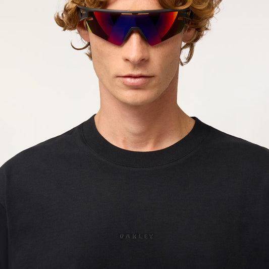Person wearing a black Oakley sweatshirt with reflective sunglasses on a light gray background