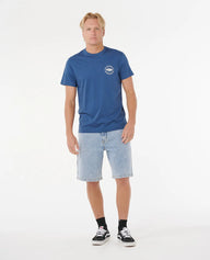 Man wearing a blue t-shirt with a logo and light blue shorts on a white background