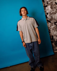 Person wearing a polo shirt with a brand logo against a blue wall.