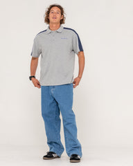 Man wearing a gray polo shirt with navy accents and blue jeans on a white background