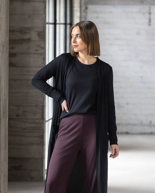 Woman wearing a black long-sleeve top and maroon pants against a concrete wall.