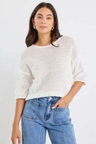 Woman wearing a white textured sweater and blue jeans against a plain background