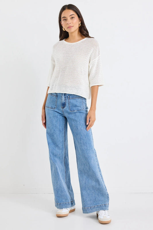 Woman wearing a white textured top and blue jeans on a white background