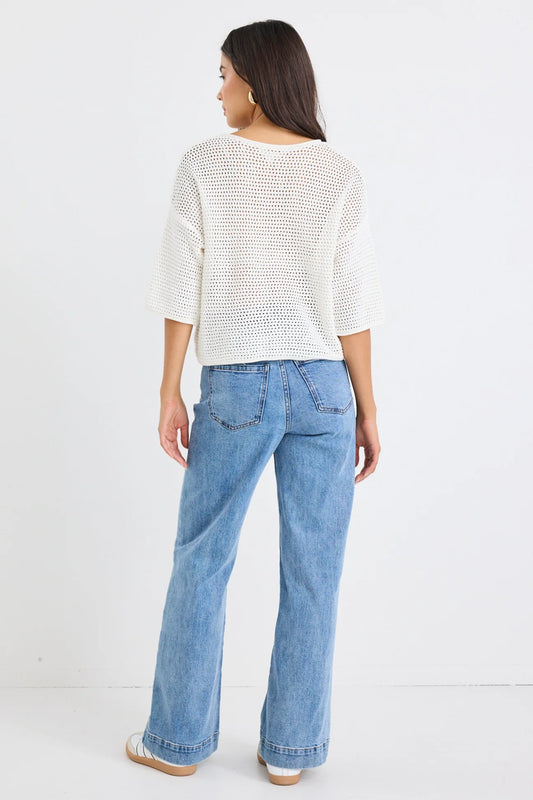 Woman wearing a white textured sweater and blue jeans on a white background